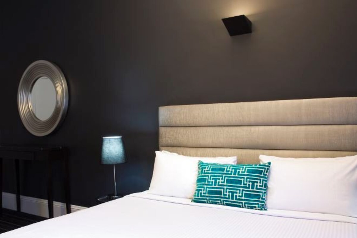 A hotel room with a large bed, a round mirror on the wall, and a nightstand with a lamp.