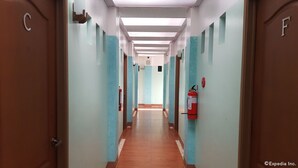 A long, narrow hallway with light blue walls and wooden floors. There are doors labeled with letters on either side.
