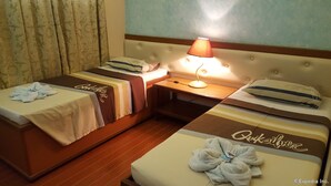A hotel room with two beds, each with a branded duvet cover, a bedside table with a lamp, and a window with curtains.
