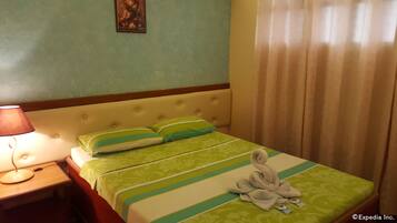 Una habitación de hotel con cama, mesita de noche, lámpara y ventana con cortinas.