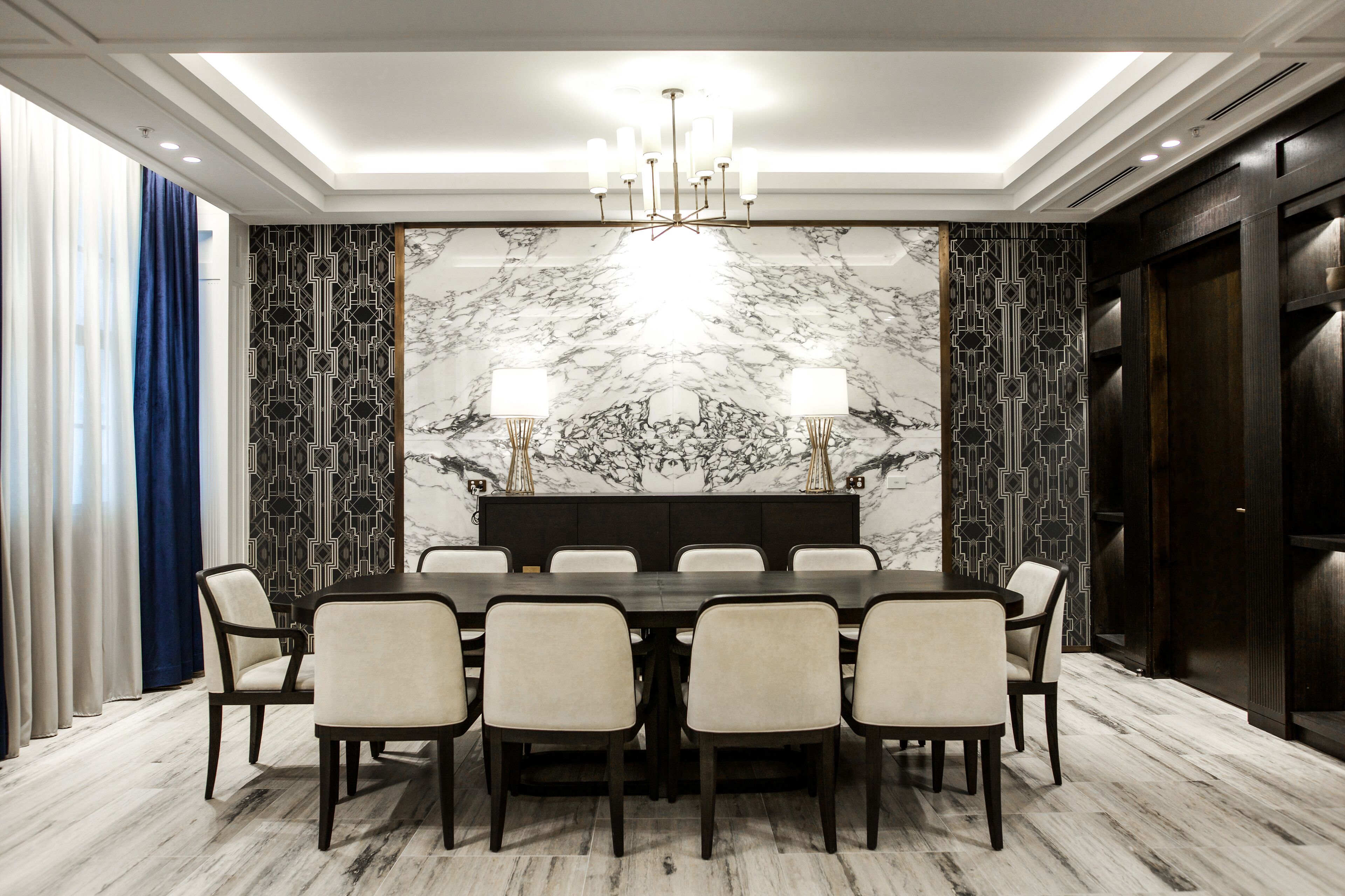 Comedor con pared de mármol, una araña y una mesa de madera oscura con seis sillas.