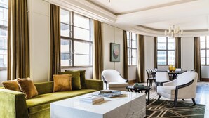 Un salón amplio con un sofá verde, sillones blancos, una mesa de centro de mármol y una zona de comedor con mesa y sillas.