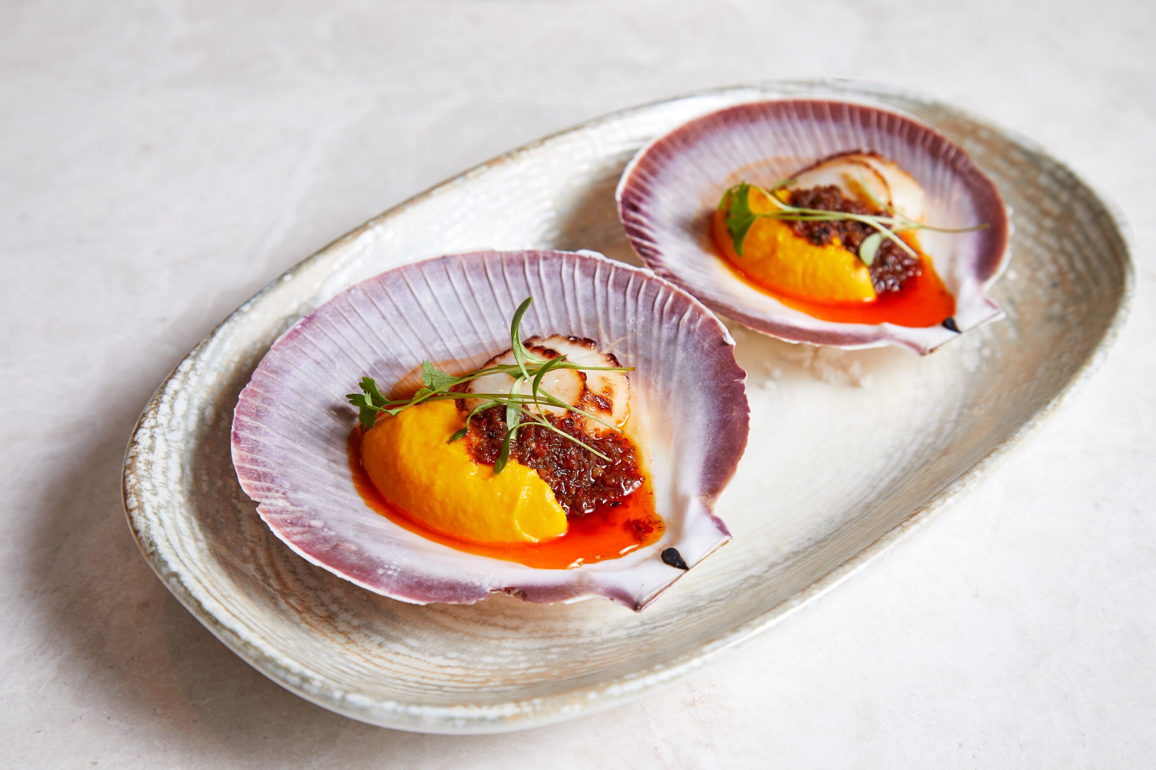 Deux coquilles Saint-Jacques servies dans une assiette en céramique rustique.