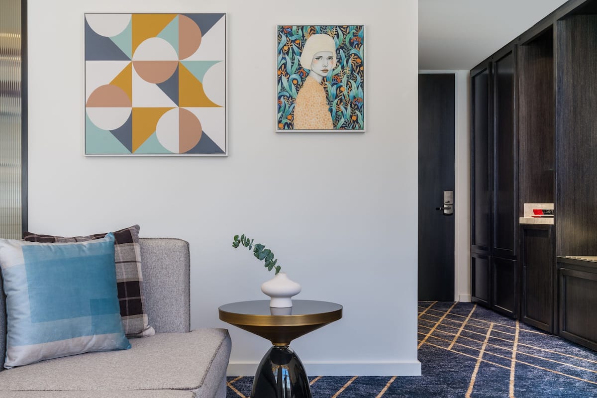 A modern living room with a sofa, a small side table with a vase, and two artworks on the wall.