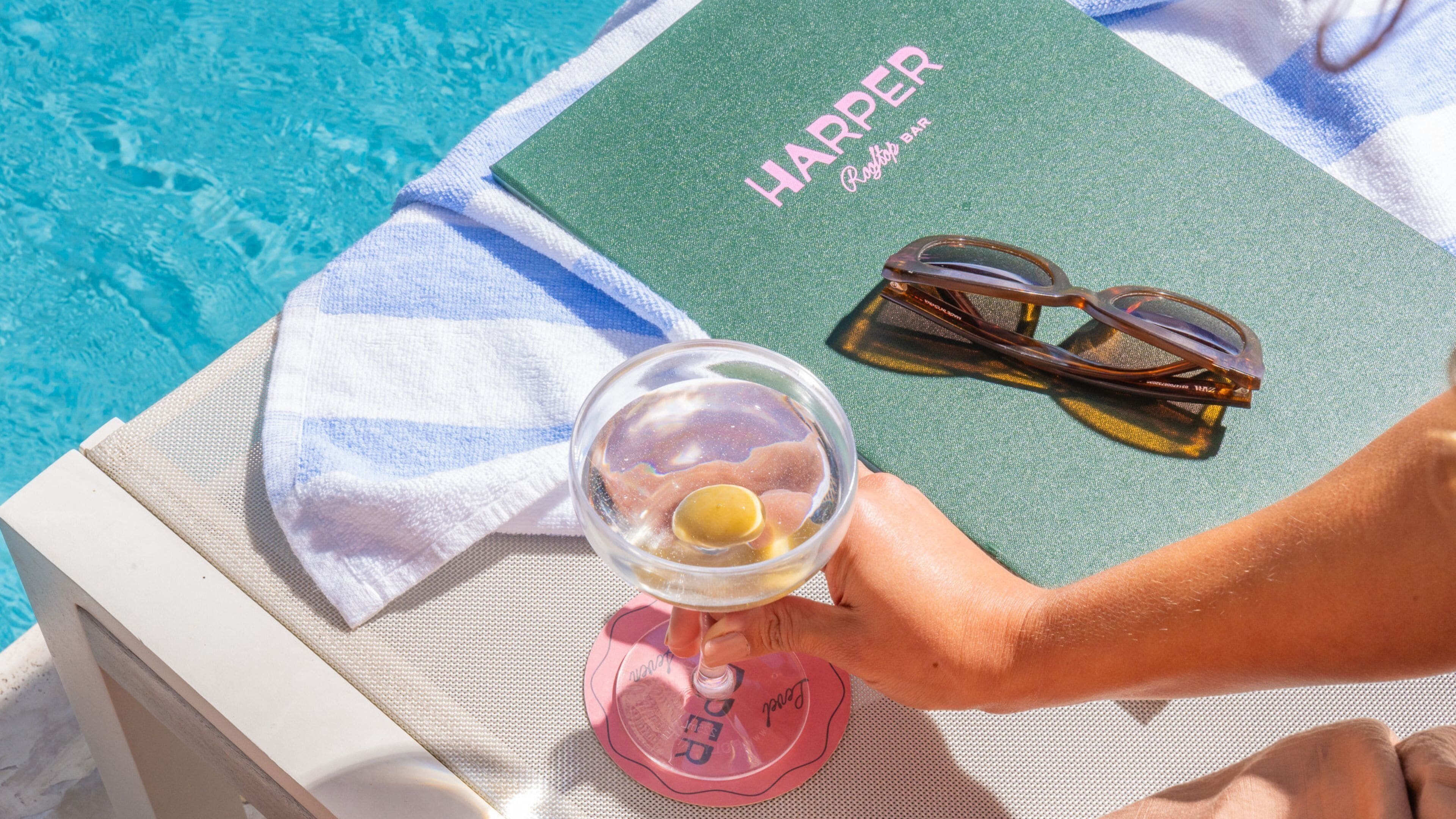 A poolside setting with a book titled 'HAPPER' and sunglasses on a towel.