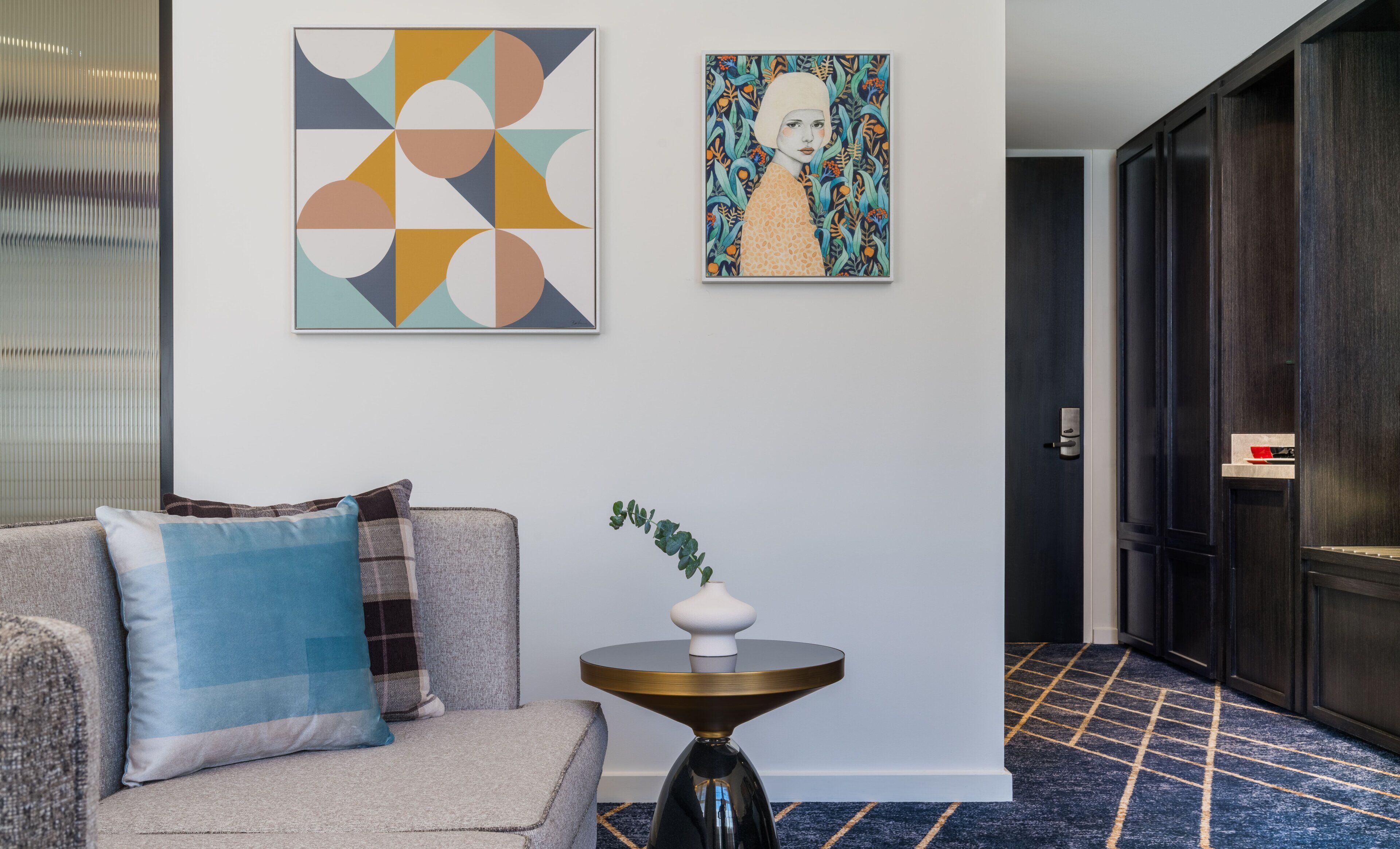 A modern interior with a sofa, a small table with a vase, and two artworks on the wall.