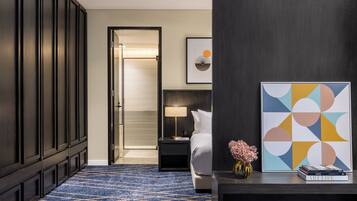 Een hotelkamer met een bed, nachtkastje, lamp, een kunstwerk met abstracte vormgeving en een vaas met bloemen.
