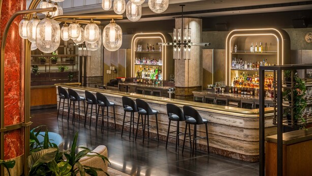 Una zona de bar moderna con mostrador de mármol, taburetes negros y una variedad de botellas y vasos en estanterías.
