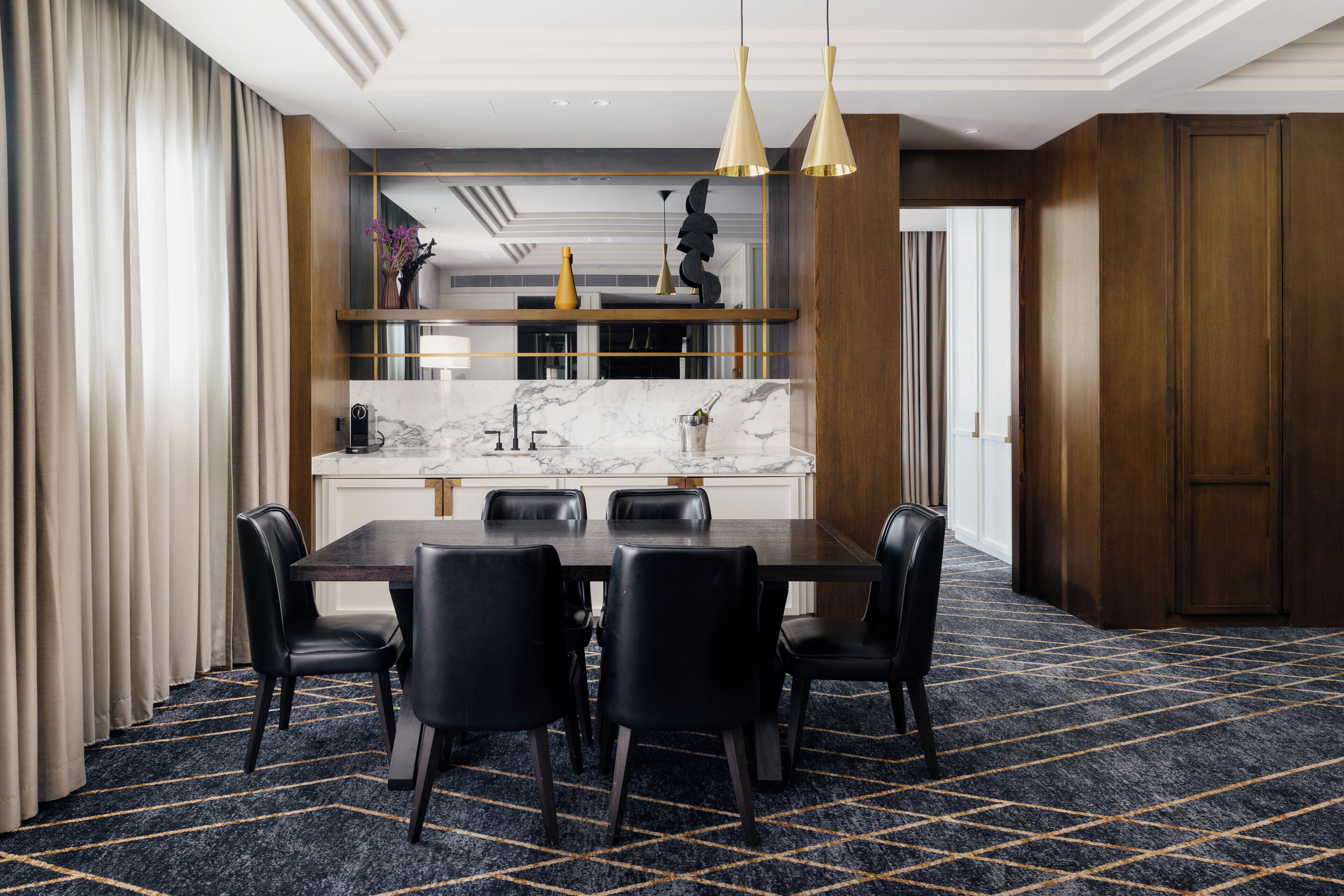 A modern dining area with a marble countertop, black chairs, and gold pendant lights.
