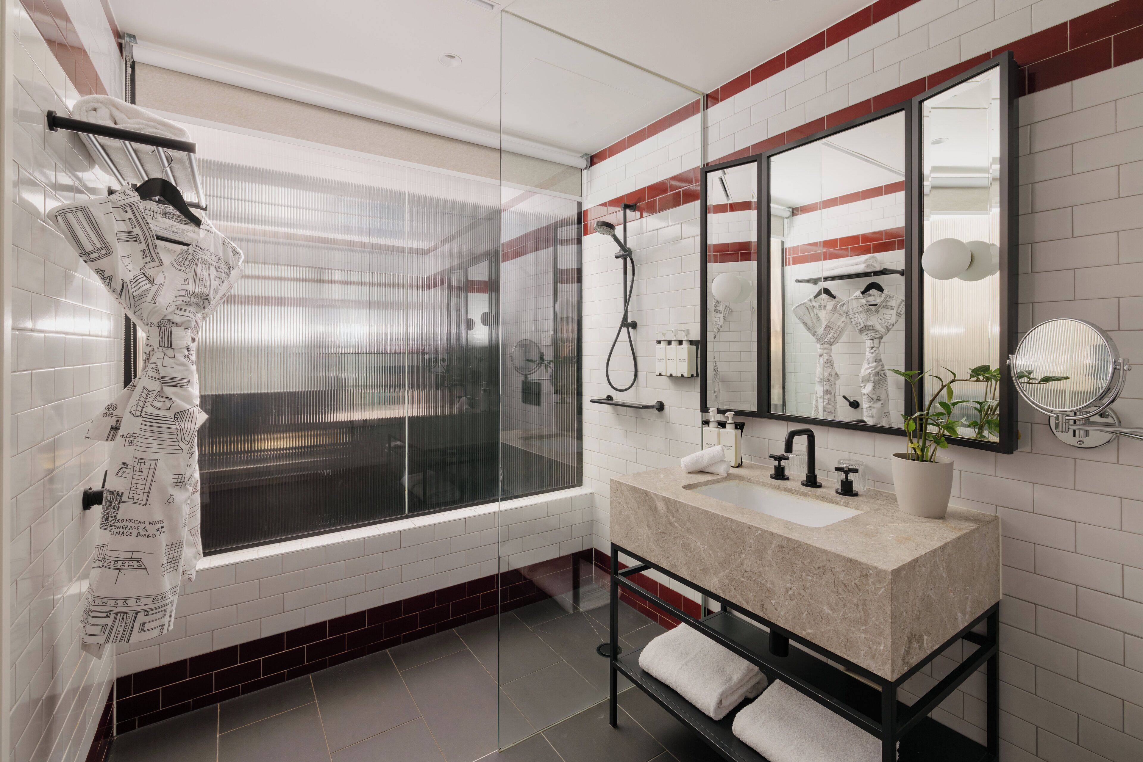Un baño moderno con un ventanal grande, cabina de ducha de vidrio, lavamanos de mármol y espejo con pared de acento rojo.