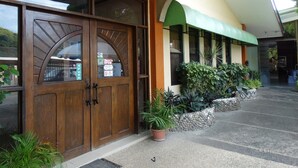 Entrada de hotel con puertas de madera dobles, un toldo verde y plantas en macetas.