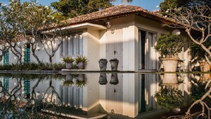 A house with a tiled roof, a white exterior, and a reflection in the water. There are potted plants and a small garden area. - Elysium (Unawatuna)