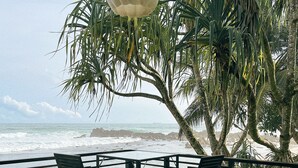 A wooden deck with chairs overlooking a beach and ocean. - Elysium (Unawatuna)