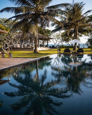 A pool with palm trees and a gazebo, surrounded by a well-maintained lawn and a view of the sea. - Elysium (Unawatuna)