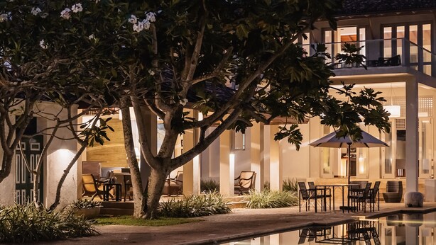 A modern building with a pool, outdoor seating, and a large tree in the foreground. - Elysium (Unawatuna)