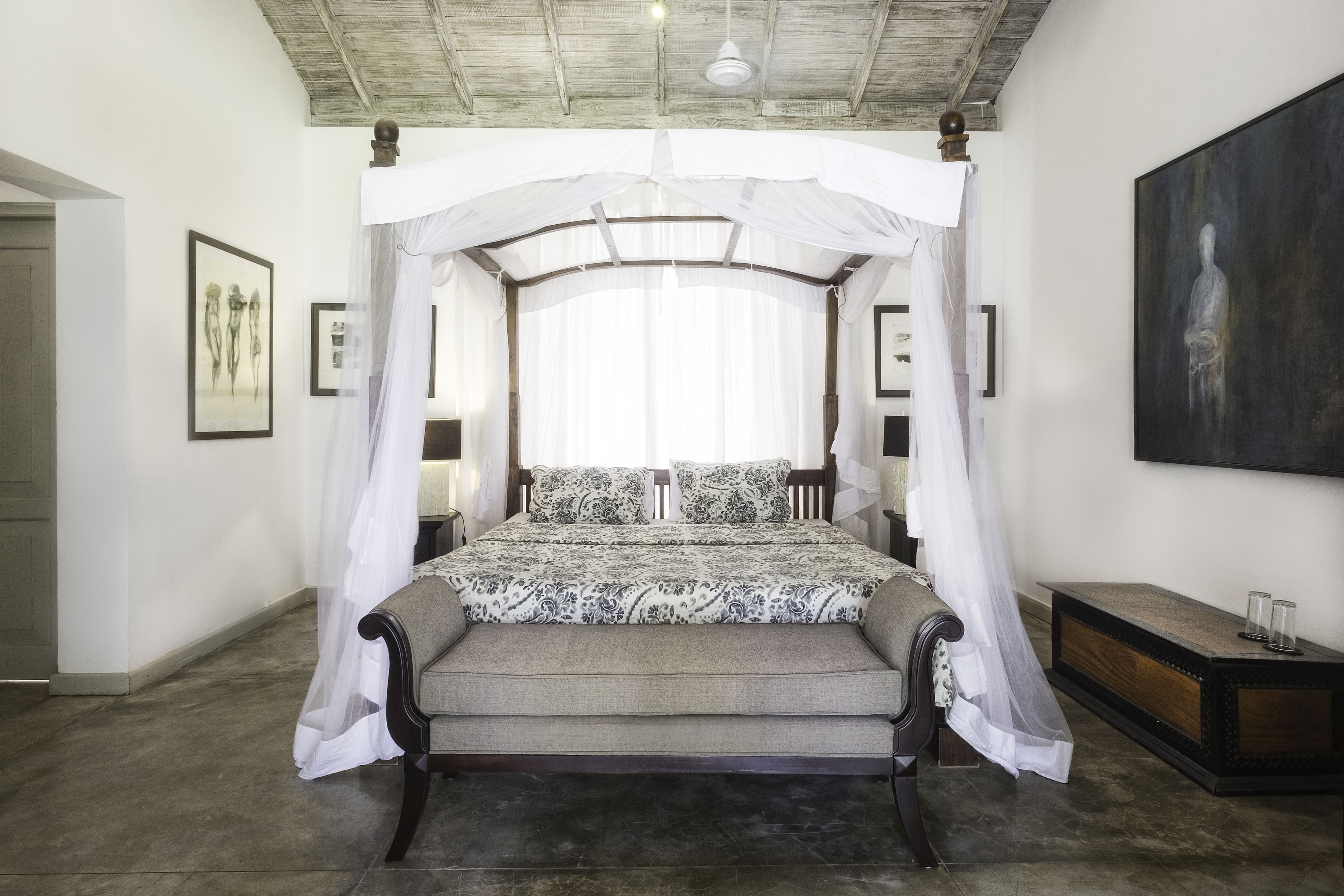 A bedroom with a canopy bed, a bedside table, and a large painting on the wall.