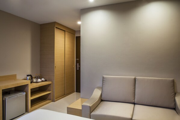 Una habitación de hotel moderna con sofá, un escritorio pequeño con hervidor, refrigerador y armario.