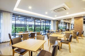 A modern dining area with tables and chairs, large windows, and a view of greenery outside. - Livotel Hotel Kaset Nawamin Bangkok (Bangkok)
