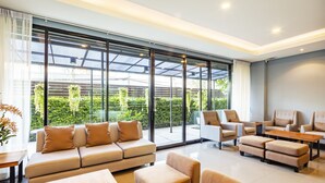 A spacious, modern lounge area with a large glass wall offering a view of greenery outside. There are several sofas and chairs arranged for seating. - Livotel Hotel Kaset Nawamin Bangkok (Bangkok)