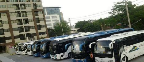 A row of buses parked in a lot with a building in the background.