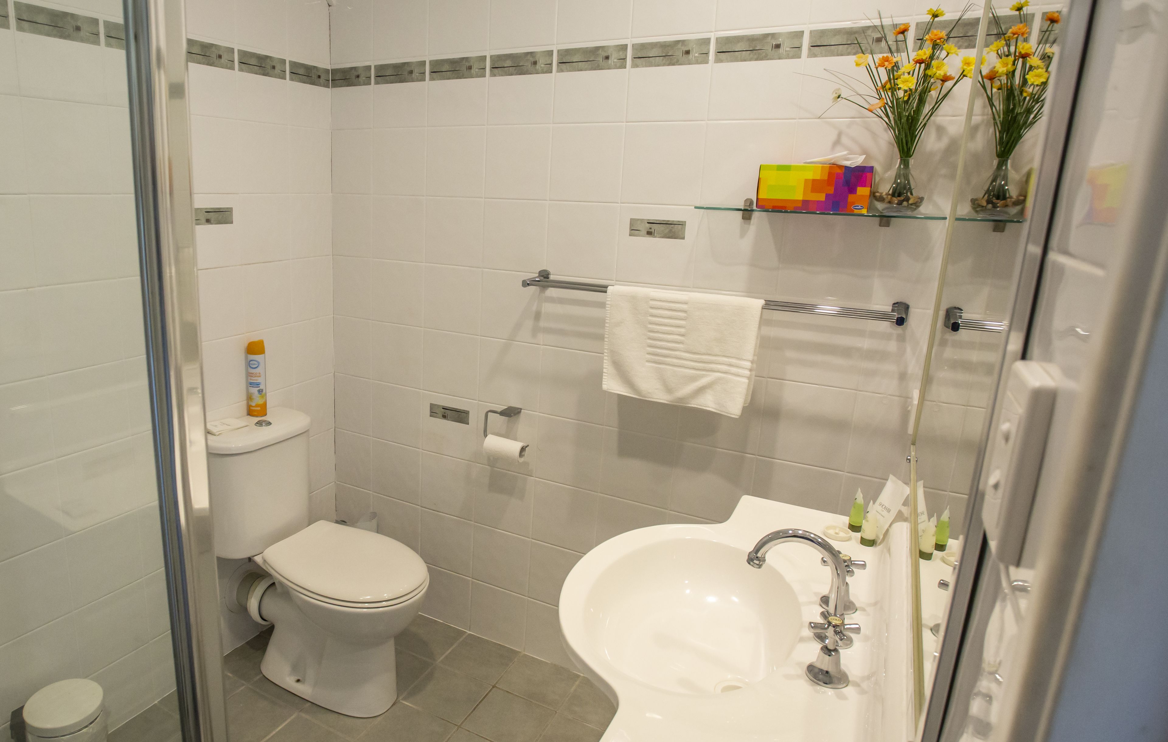 A bathroom with a toilet, sink, and shower. There are toiletries on the sink and a towel rack above the sink.
