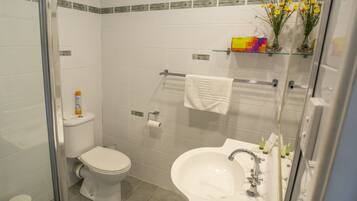 A bathroom with a toilet, sink, and shower. There are toiletries on the sink and a towel rack above the sink.