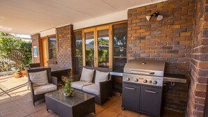 An outdoor patio with a grill, wicker furniture, and a view of the garden. - Ainslie Manor Guests House (Redcliffe)