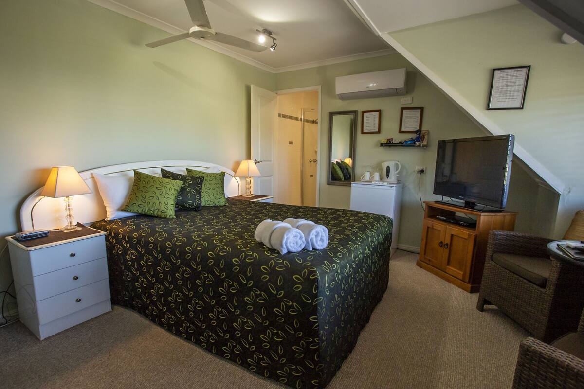 Een slaapkamer met een bed, twee nachtkastjes, een televisie, een stoel en een bureau.