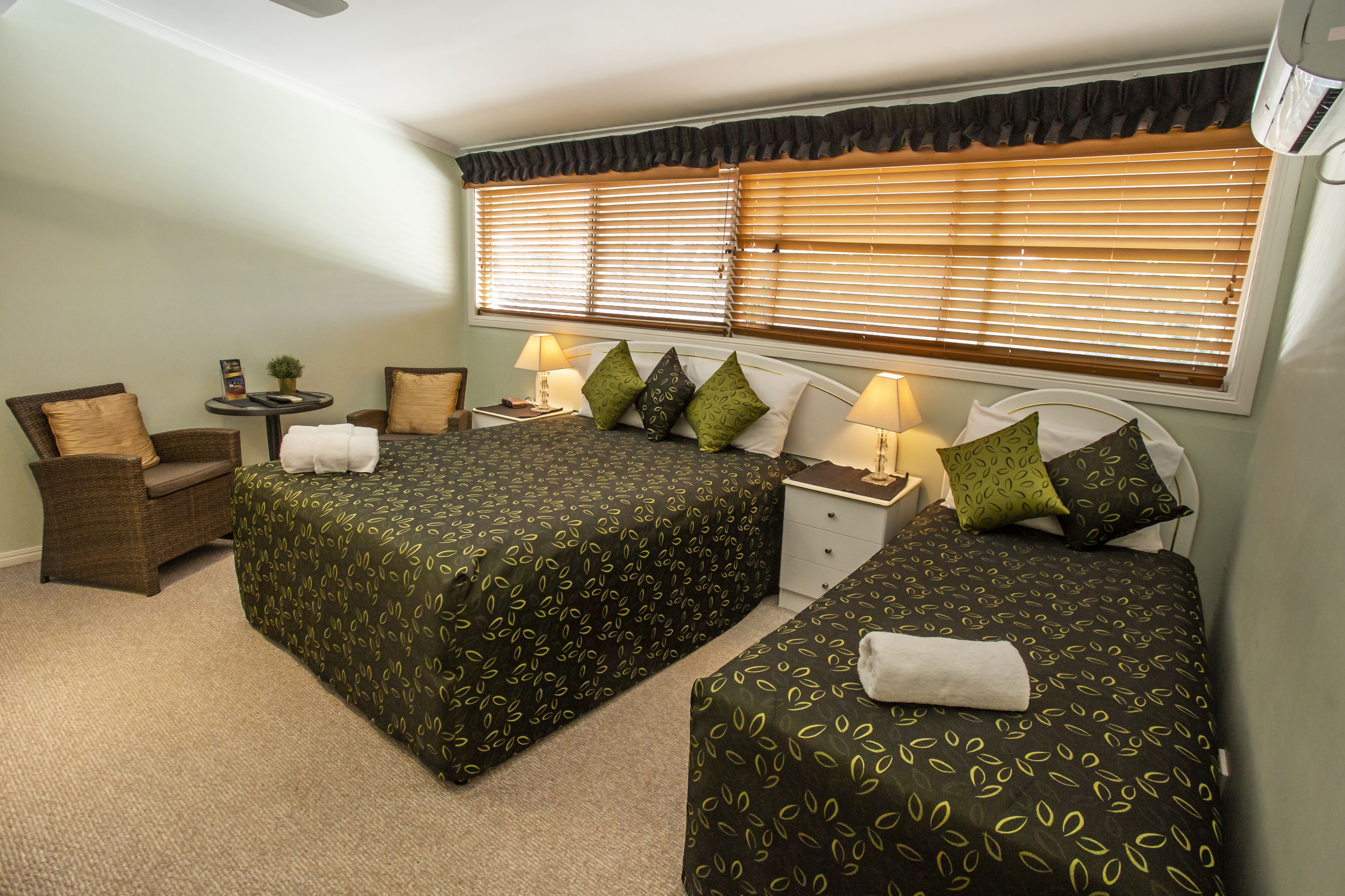 A hotel room with two beds, a chair, a nightstand, and a window with blinds.