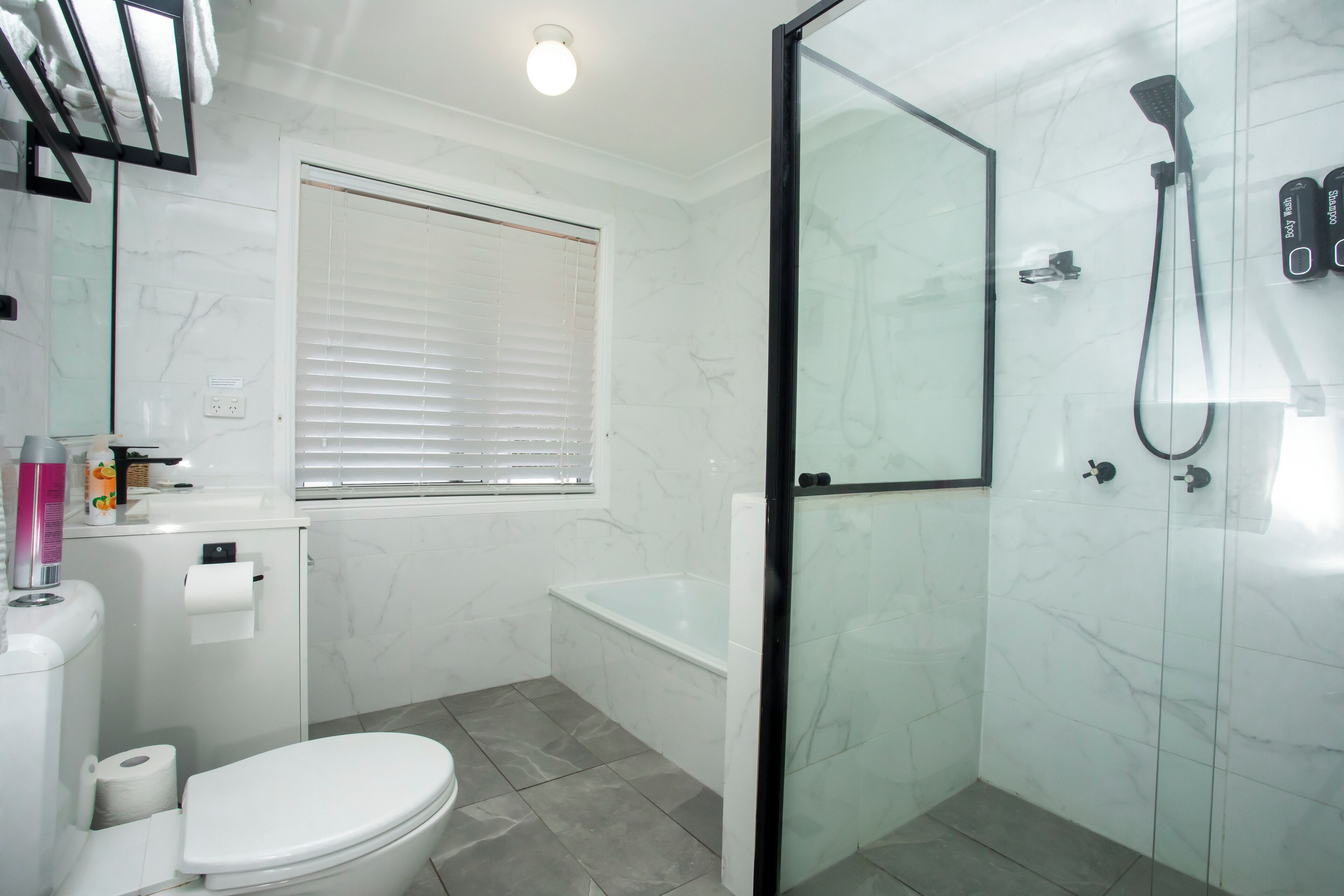 A bathroom with a toilet, a glass-enclosed shower, a bathtub, and a window with blinds.