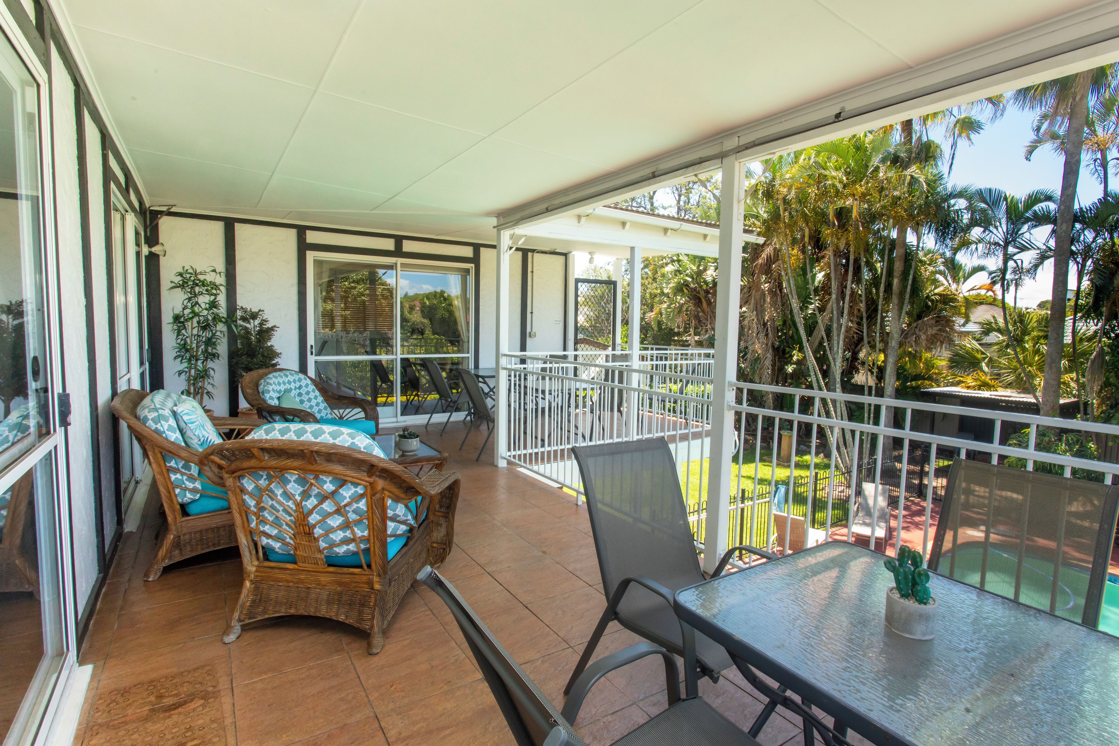 Un balcón con mobiliario de mimbre, una mesa de vidrio y vistas a la vegetación tropical.