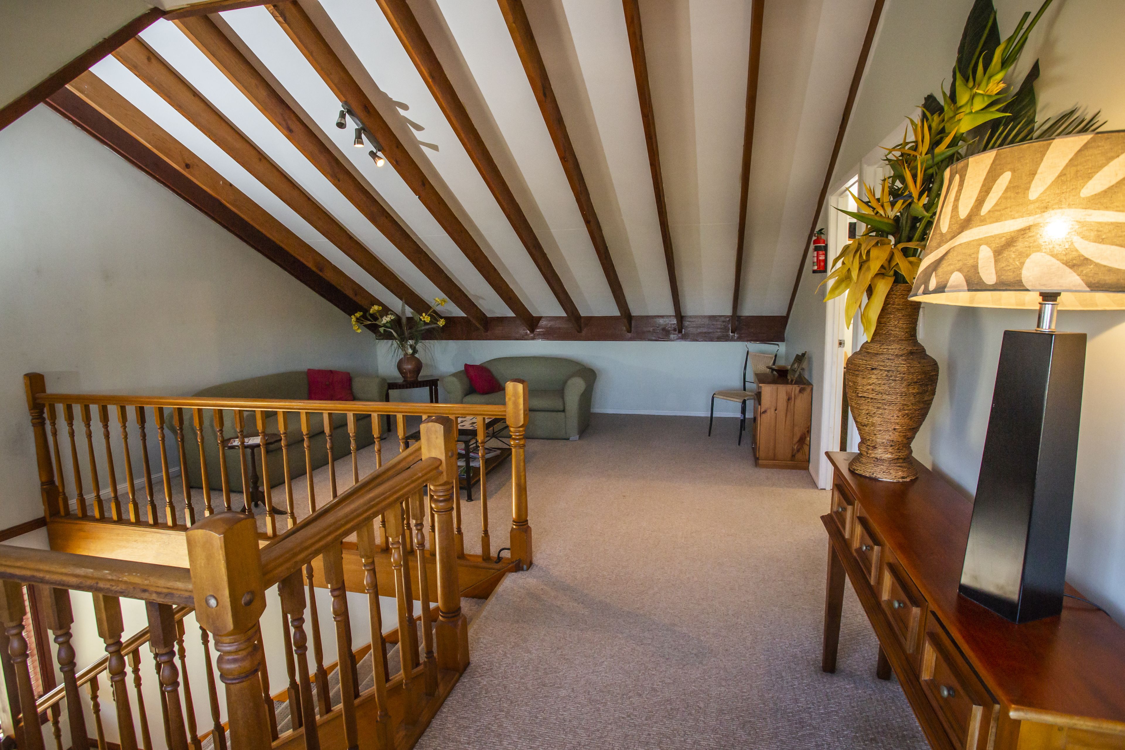 A loft-style room with a wooden staircase, a sofa, a small table, and a lamp.