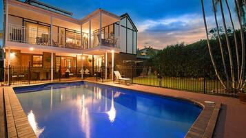 A two-story house with a swimming pool, a balcony, and a fenced yard.