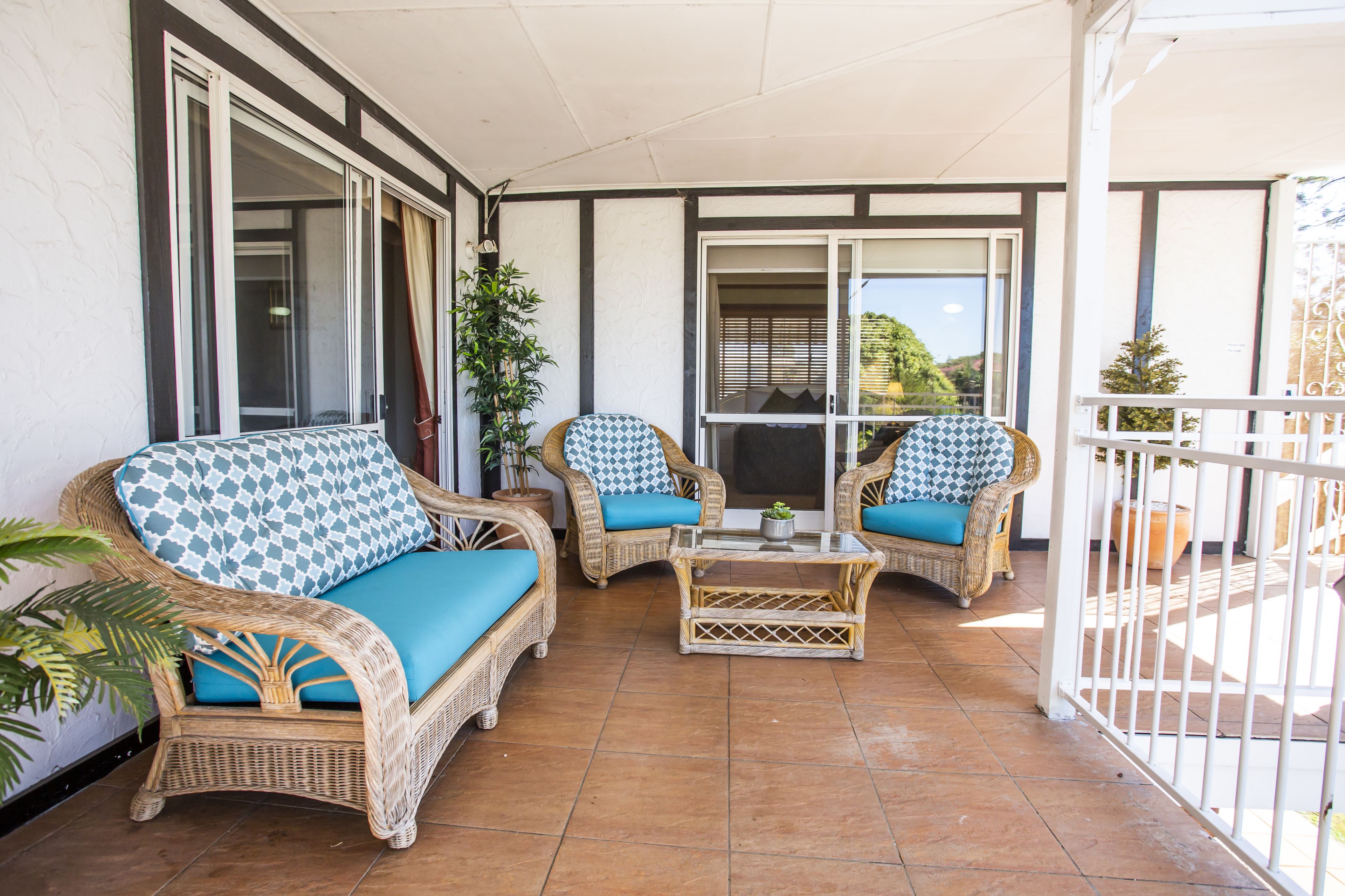 A covered patio with wicker furniture, including two sofas and a coffee table, and a view of the outdoors through a glass door.