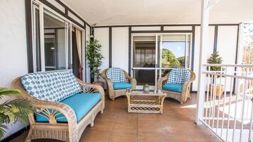 A covered patio with wicker furniture, including two sofas and a coffee table, and a view of the outdoors through a glass door.