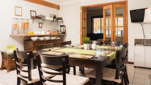 A dining area with a wooden table, chairs, and a buffet counter with food items. - Ainslie Manor Guests House (Redcliffe)