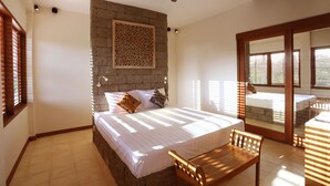Ein Schlafzimmer mit einem großen Bett, einer hölzernen Bank, einem Deckenventilator und einer Steinwand.