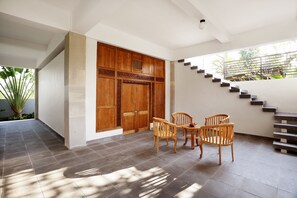A spacious room with a large wooden door, a staircase, and a dining area with wooden chairs.
