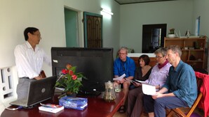 Una sala de reuniones con una mesa redonda, portátiles, documentos y una televisión.