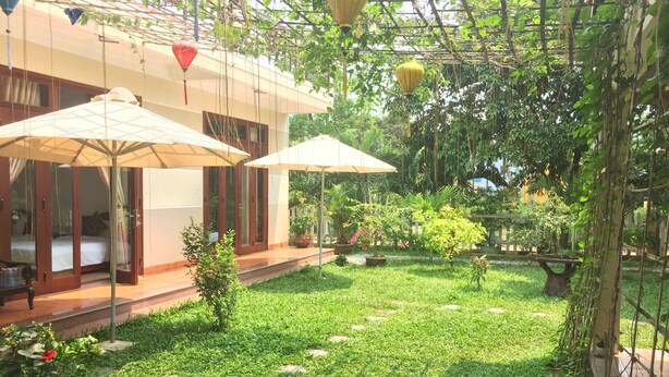 Un patio con una cama, dos sombrillas y un jardín.