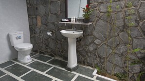 Un baño con pared de piedra, un lavamanos pedestal blanco y un inodoro.
