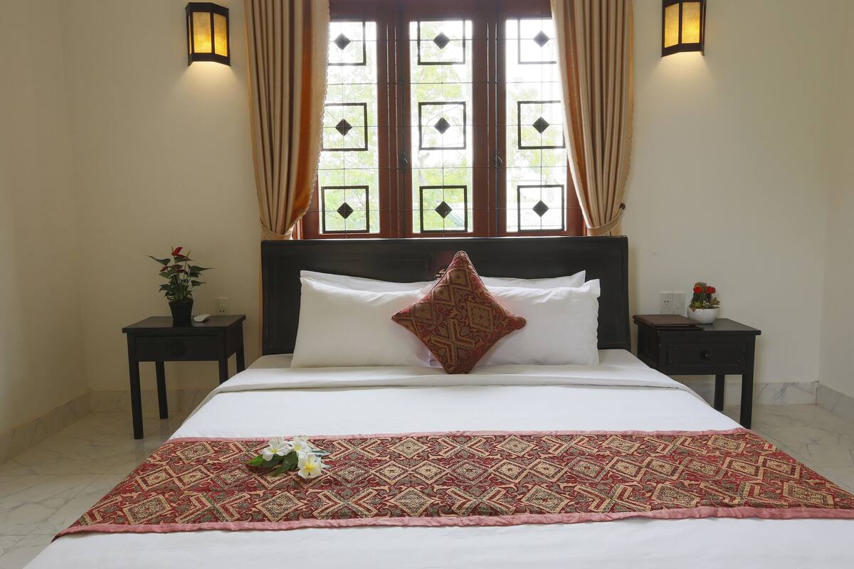 A neatly made bed with a patterned bedspread, two bedside tables with lamps, and a window with curtains.