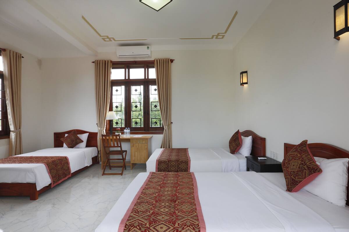 A hotel room with two single beds, a desk, a chair, and a window with curtains.