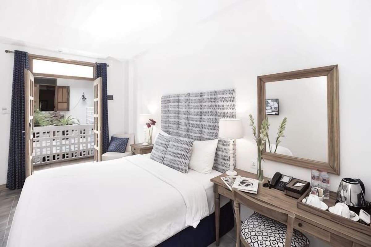 Habitación de hotel con una cama grande, un escritorio con teléfono, un espejo y vistas a través de una puerta abierta.