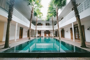 A pool area with a clear view of the water, surrounded by palm trees and wooden flooring.