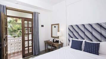 Hotelkamer met een bed, een bureau met telefoon en lamp, een spiegel en uitzicht op palmbomen door een deur.