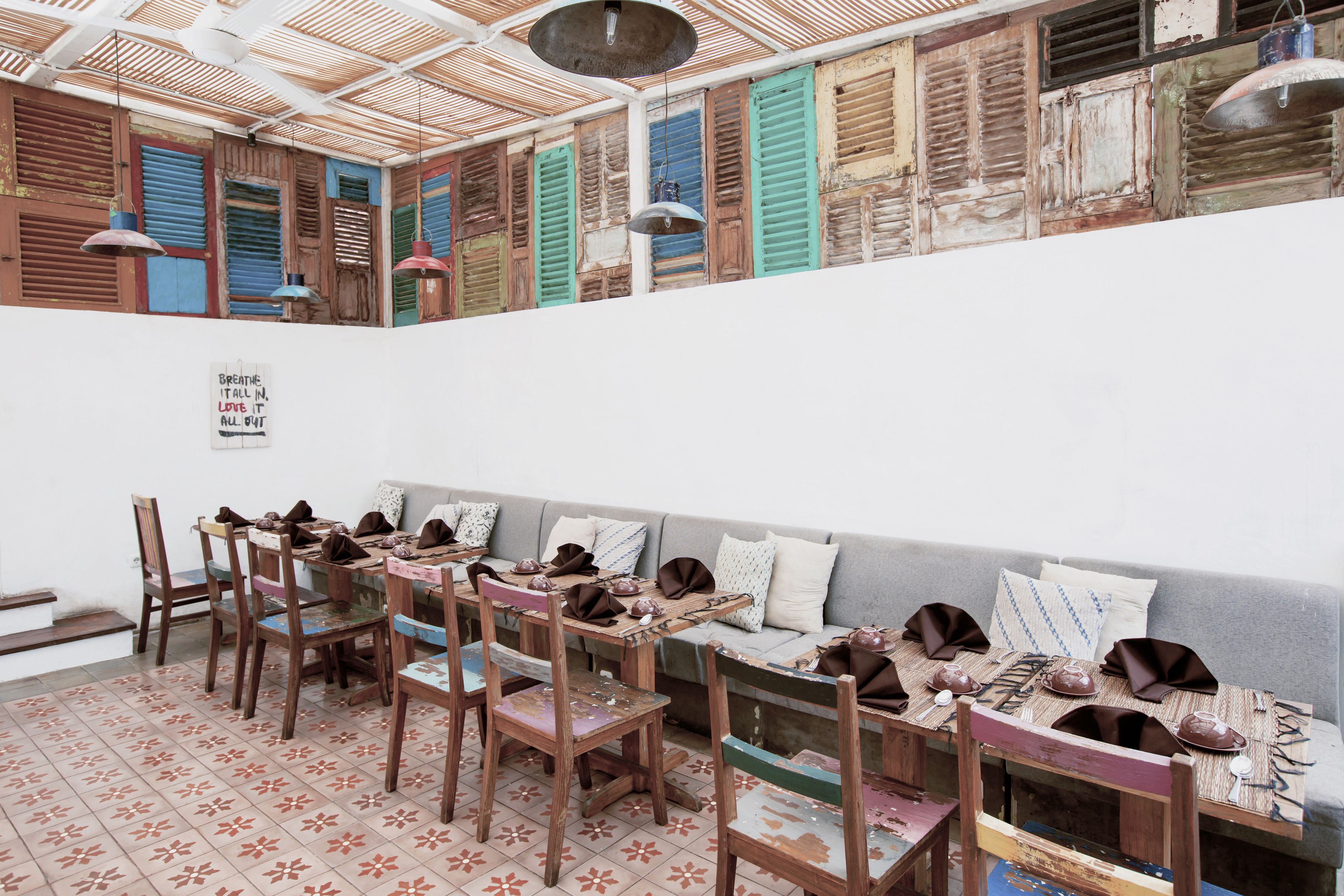 A dining area with wooden tables and chairs, a sofa, and a ceiling with wooden slats.