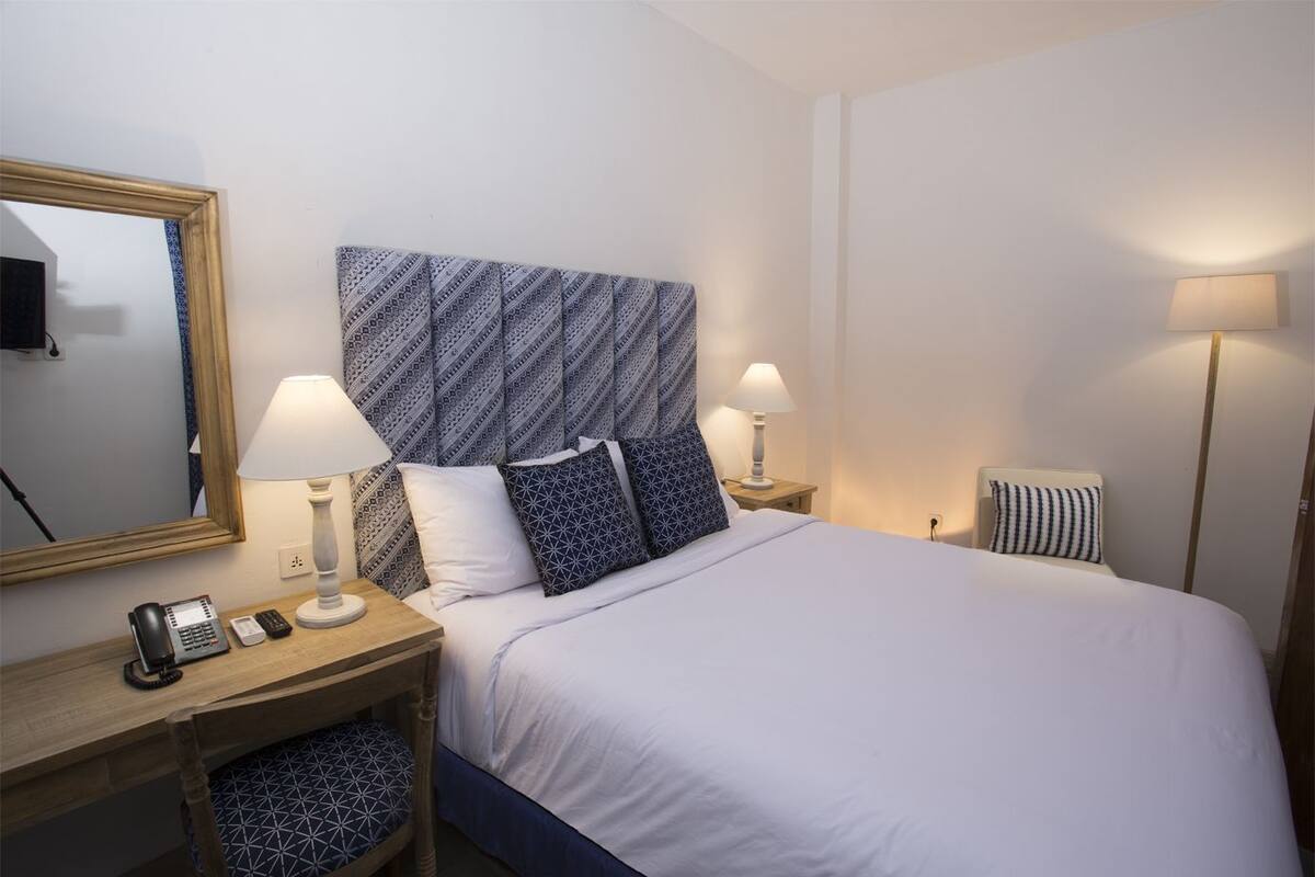 Ett hotellrum med en säng, två sängbord, en telefon, en lampa och en spegel.