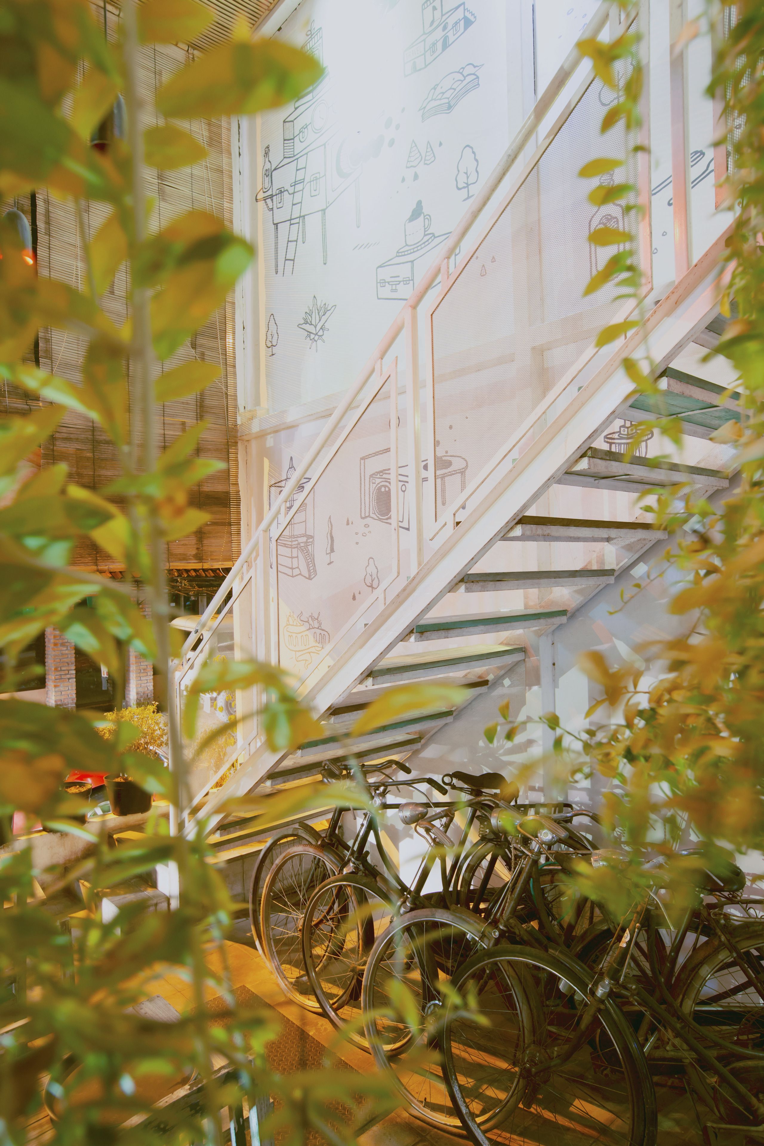 Een trap met een glazen leuning en een muur met illustraties. Fietsen staan in de buurt van de trap geparkeerd.