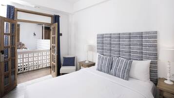 Un dormitorio con una cama grande, cabecera de madera, una mesita de noche, una silla y vistas a través de un puerta abierta.